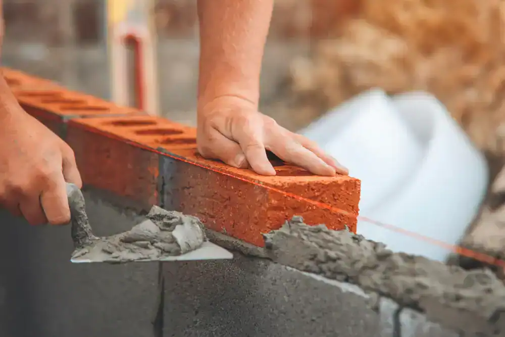 Close-up of a person laying red bricks with mortar on a wall, using a trowel and aligning the bricks with a taut guideline&mdash;showcasing expert craftsmanship by an NJ construction company in Morris & Essex County.