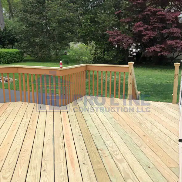 A freshly constructed wooden deck with railings, built by a top construction company in Morris & Essex County, NJ, overlooks a green backyard with trees and grass; a drink bottle sits on the railing.